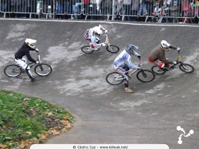 Coupe des Lacs 2009 de BMX, manche de Cran-Gevrier - le dim. 08.11.2009. 5e et avant-dernière manche de cette compétition franco-suisse de BMX. – Les trajectoires de chaque participant ne sont pas forcément compatibles avec celles des autres... Le pilote en bleu avec la veste de pluie va devoir corriger un peu le tir (!)... – « Coupe des Lacs 2009 de BMX, manche de Cran-Gevrier » – 5e manche de la Coupe des Lacs sur la piste de bicross de Cran-Gevrier. – mots associés : bmx, coupe des lacs